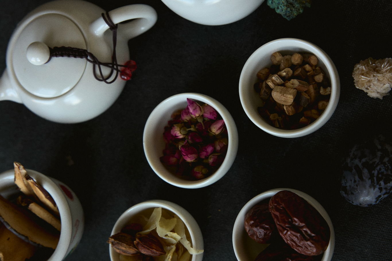 Herbal ingredients and a white teapot arranged on a dark table